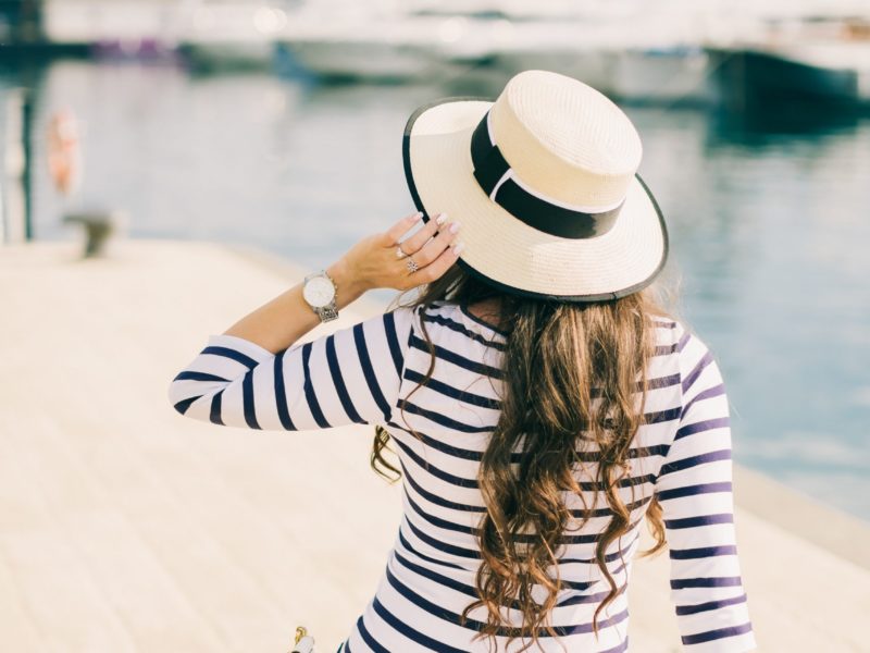 woman in summer dress with hat on the beach. Fashion girl travel. Back view. Yachts background